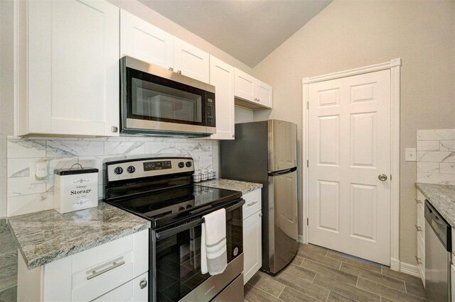 kitchen featuring light stone countertops, tasteful backsplash, stainless steel appliances, vaulted ceiling, and white cabinetry