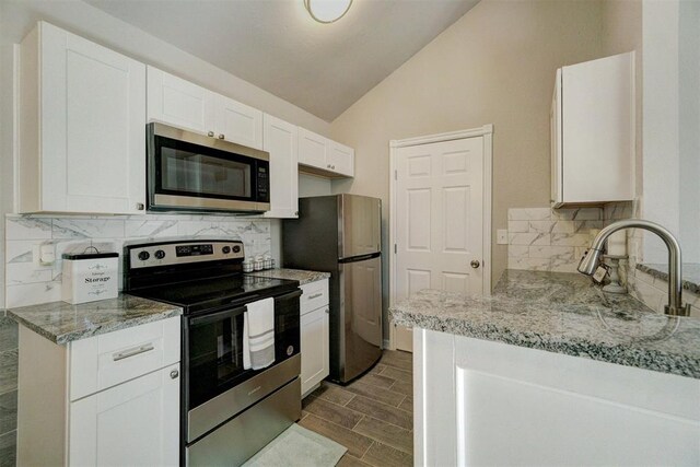 kitchen featuring light stone countertops, stainless steel appliances, vaulted ceiling, decorative backsplash, and white cabinets