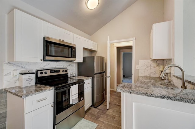 kitchen featuring vaulted ceiling, tasteful backsplash, light stone counters, white cabinetry, and stainless steel appliances