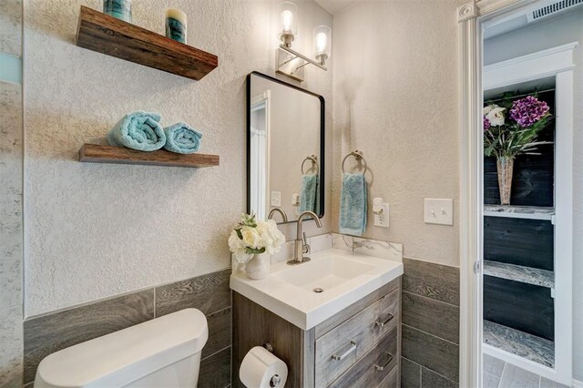 bathroom with vanity, toilet, and tile walls