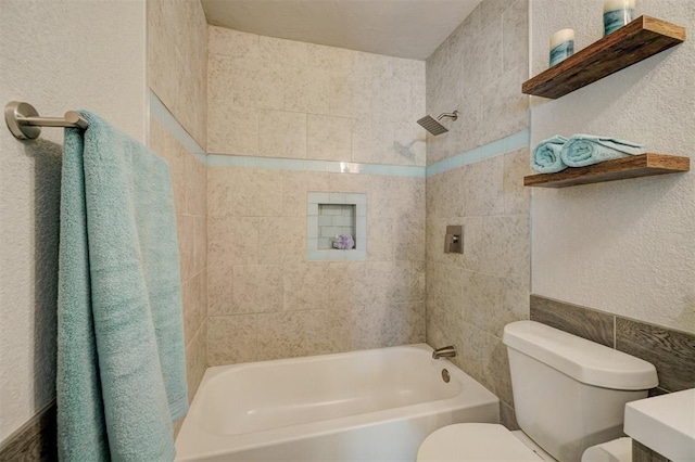 bathroom featuring tiled shower / bath combo, toilet, and tile walls