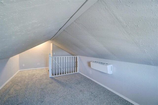 additional living space with a textured ceiling, a wall mounted AC, carpet, and vaulted ceiling