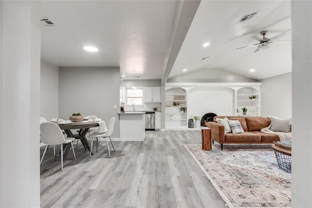 living room featuring ceiling fan, sink, light hardwood / wood-style flooring, vaulted ceiling, and a fireplace