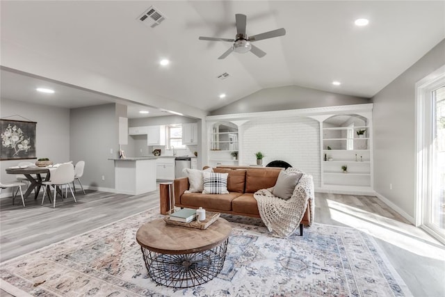 living room with built in shelves, light hardwood / wood-style flooring, ceiling fan, and sink