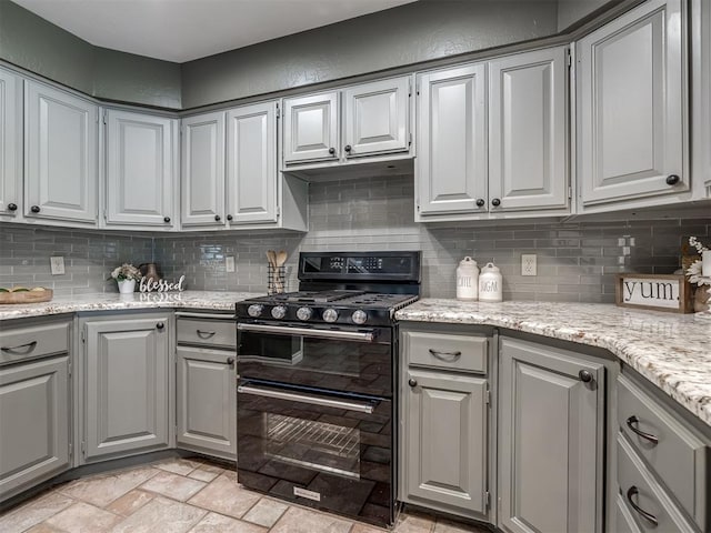 kitchen featuring light stone countertops, black gas range, backsplash, and gray cabinetry