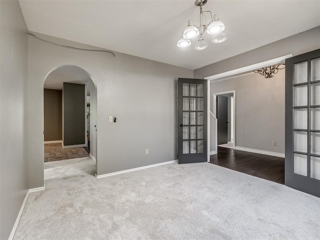 unfurnished room featuring french doors, carpet floors, and an inviting chandelier