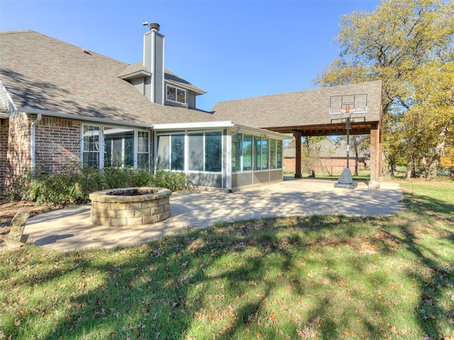 rear view of property with a lawn, a sunroom, a patio, and a fire pit