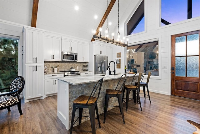 kitchen with a kitchen island with sink, high vaulted ceiling, white cabinets, appliances with stainless steel finishes, and a breakfast bar area