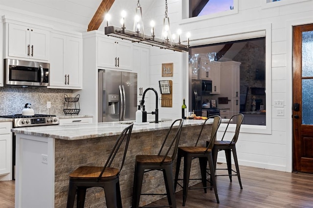 kitchen with a kitchen breakfast bar, white cabinets, an island with sink, and appliances with stainless steel finishes