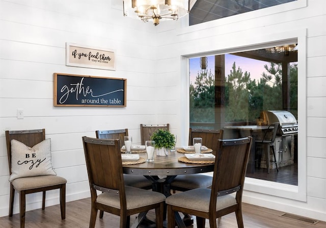 dining space featuring hardwood / wood-style flooring, wood walls, and an inviting chandelier