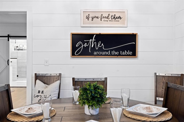 dining space with a barn door, hardwood / wood-style flooring, and wooden walls