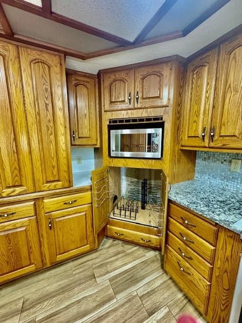 kitchen featuring stainless steel microwave, tasteful backsplash, light stone counters, a textured ceiling, and light wood-type flooring