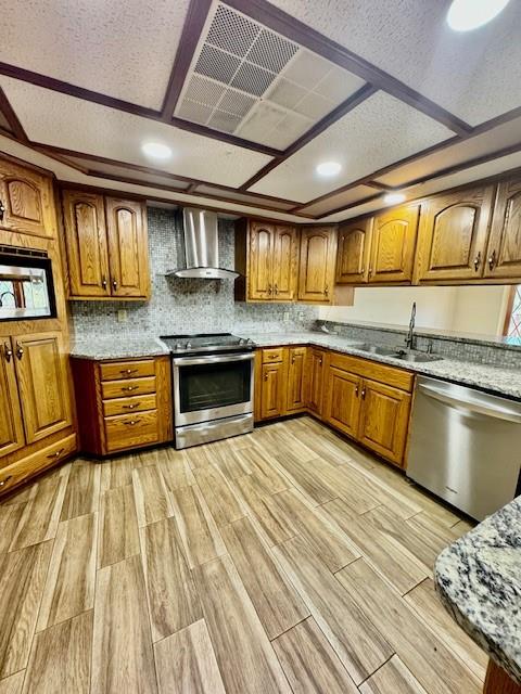 kitchen featuring wall chimney range hood, sink, light hardwood / wood-style flooring, appliances with stainless steel finishes, and light stone counters