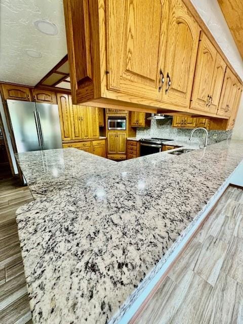 kitchen featuring sink, wooden walls, light hardwood / wood-style flooring, light stone counters, and stainless steel appliances