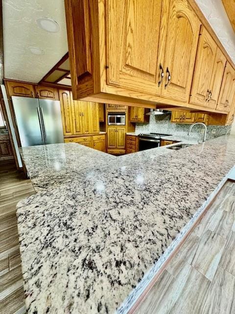 kitchen featuring wall chimney range hood, sink, light stone countertops, appliances with stainless steel finishes, and light hardwood / wood-style floors