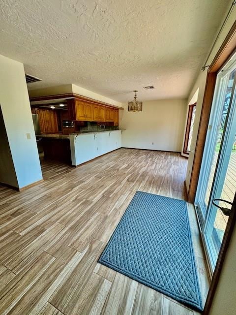 interior space with kitchen peninsula, light hardwood / wood-style flooring, hanging light fixtures, and a healthy amount of sunlight