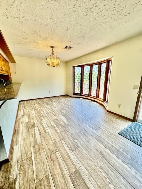 unfurnished living room with a chandelier, a textured ceiling, and light hardwood / wood-style flooring