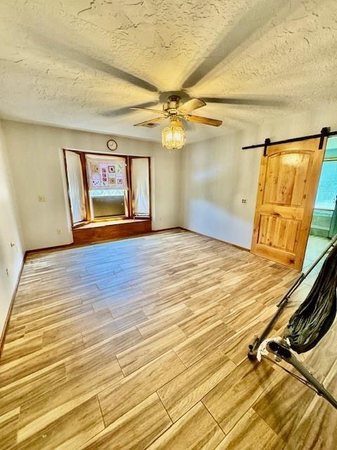 interior space featuring a textured ceiling, a barn door, hardwood / wood-style flooring, and ceiling fan