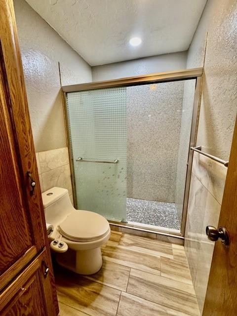 bathroom with hardwood / wood-style flooring, toilet, a shower with door, and a textured ceiling