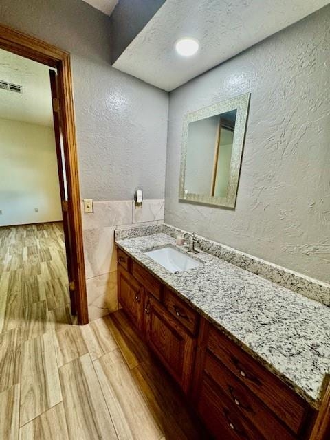 bathroom featuring wood-type flooring, vanity, a textured ceiling, and tile walls