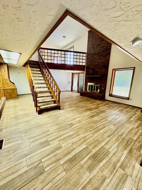 unfurnished living room featuring wood-type flooring, a textured ceiling, and high vaulted ceiling