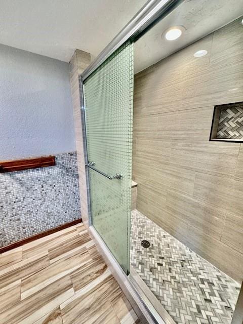 bathroom featuring a shower with door, wood-type flooring, and tile walls