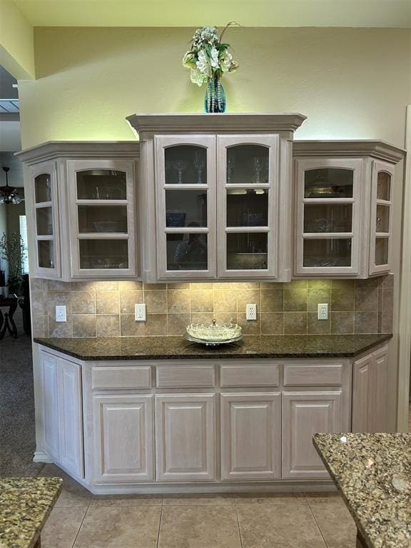 bar featuring decorative backsplash, white cabinets, dark stone counters, and light tile patterned floors