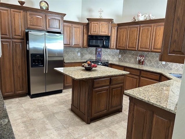 kitchen with a center island, light stone counters, decorative backsplash, light tile patterned flooring, and black appliances