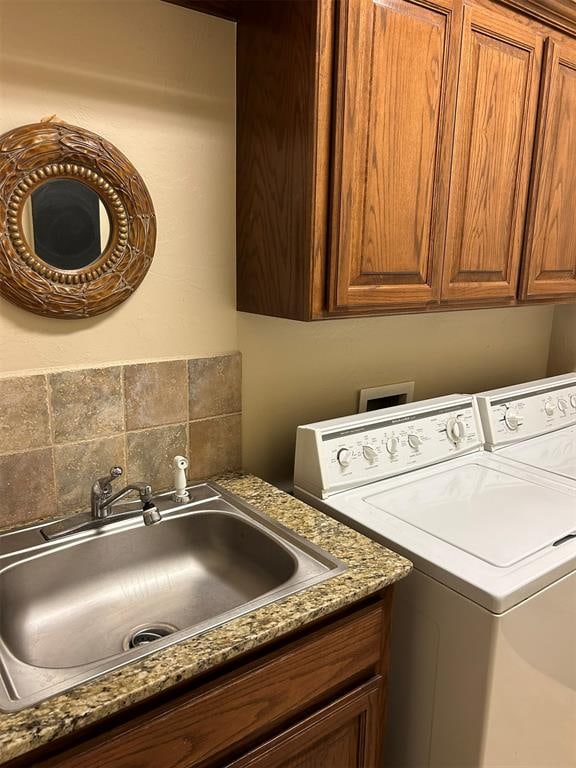 clothes washing area featuring washing machine and dryer, sink, and cabinets