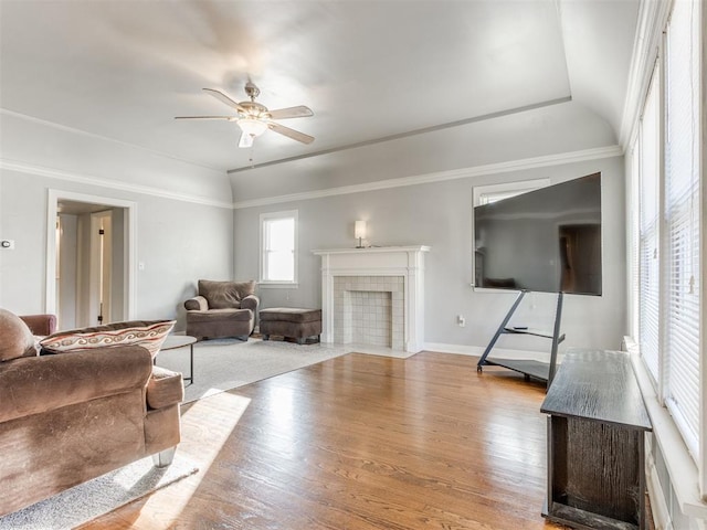 living room featuring a tray ceiling, a fireplace, ceiling fan, light hardwood / wood-style floors, and crown molding