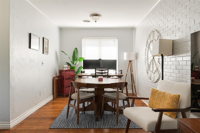 dining area featuring brick wall, wood-type flooring, and ornamental molding