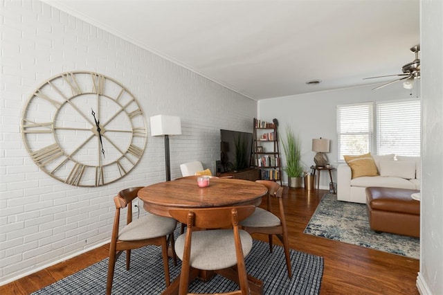 dining room with ceiling fan, dark wood-type flooring, and brick wall