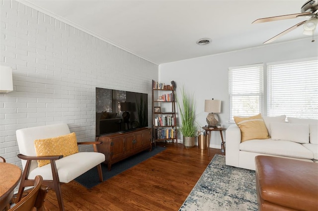 living room with brick wall, dark hardwood / wood-style flooring, ceiling fan, and crown molding