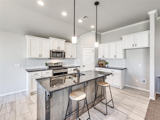 kitchen featuring ornamental molding, dark stone counters, stainless steel appliances, sink, and a center island with sink