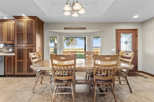 tiled dining room with a raised ceiling, a healthy amount of sunlight, and a notable chandelier