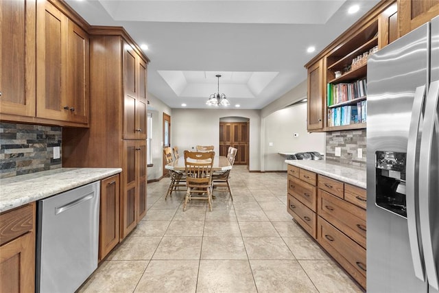 kitchen featuring light stone countertops, appliances with stainless steel finishes, tasteful backsplash, a raised ceiling, and pendant lighting