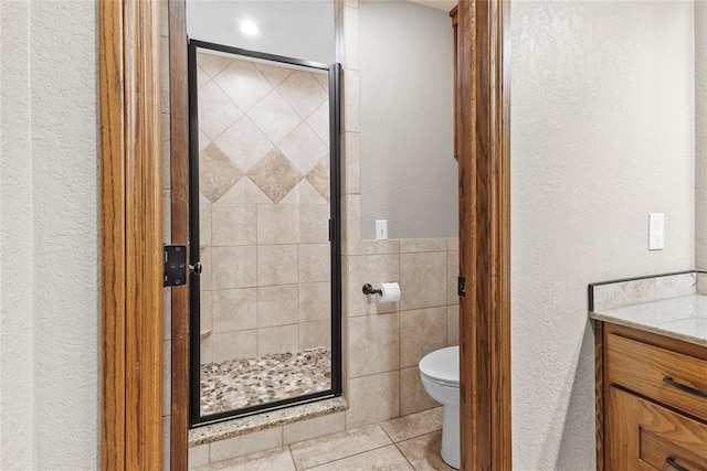 bathroom featuring tile patterned floors, toilet, a shower with door, vanity, and tile walls