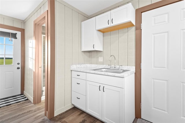 kitchen featuring wooden walls, sink, white cabinets, and wood-type flooring