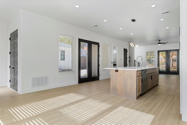 kitchen featuring french doors, stainless steel dishwasher, decorative light fixtures, light hardwood / wood-style flooring, and an island with sink