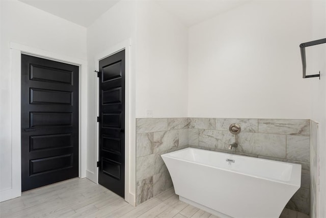 bathroom with a bath, tile walls, and hardwood / wood-style floors