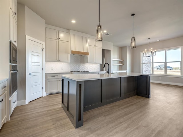 kitchen with a kitchen island with sink, an inviting chandelier, white cabinets, light wood-type flooring, and appliances with stainless steel finishes