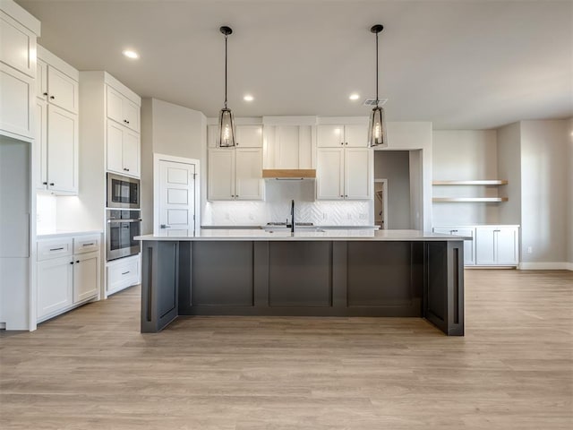 kitchen featuring appliances with stainless steel finishes, a kitchen island with sink, decorative light fixtures, light hardwood / wood-style flooring, and white cabinets