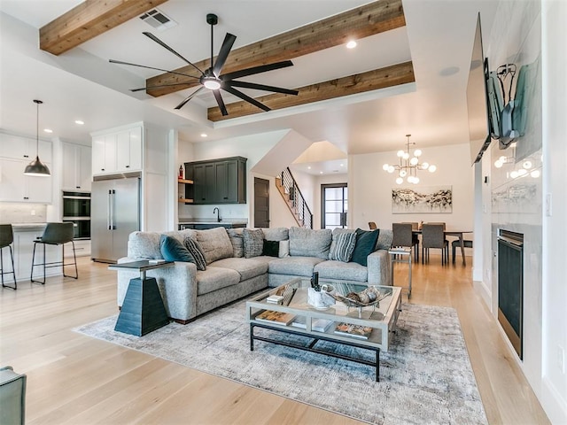 living room with beamed ceiling, ceiling fan with notable chandelier, and light wood-type flooring