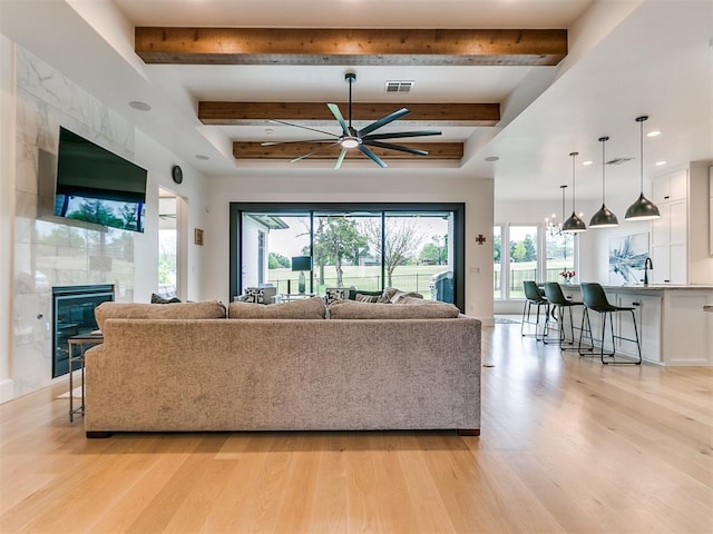 living room featuring a tiled fireplace, light hardwood / wood-style floors, and ceiling fan with notable chandelier