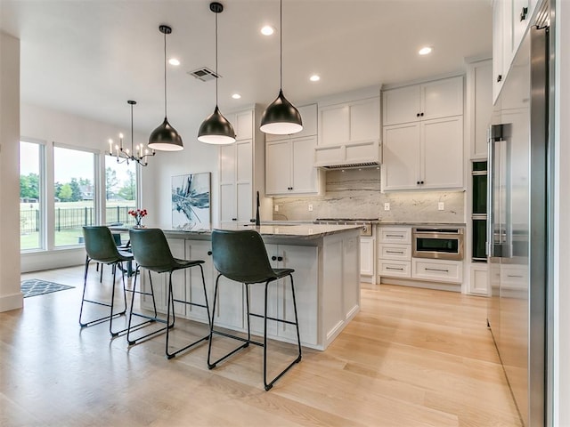 kitchen featuring light stone counters, stainless steel appliances, a kitchen island with sink, pendant lighting, and white cabinets