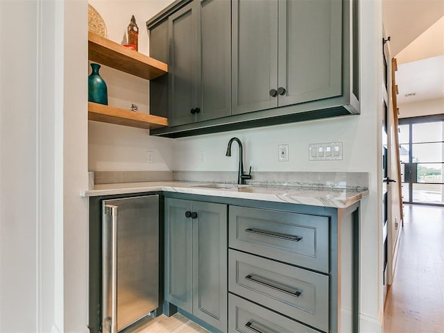 kitchen featuring stainless steel fridge, light stone counters, light hardwood / wood-style flooring, and sink