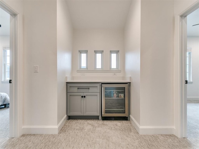 bar featuring a wealth of natural light, gray cabinets, light carpet, and wine cooler