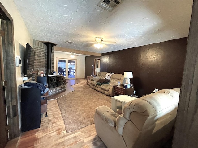 living room featuring ceiling fan, wood-type flooring, a wood stove, and a textured ceiling