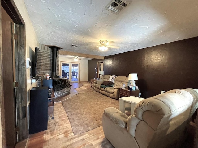 living room with wood-type flooring, a textured ceiling, a wood stove, and ceiling fan