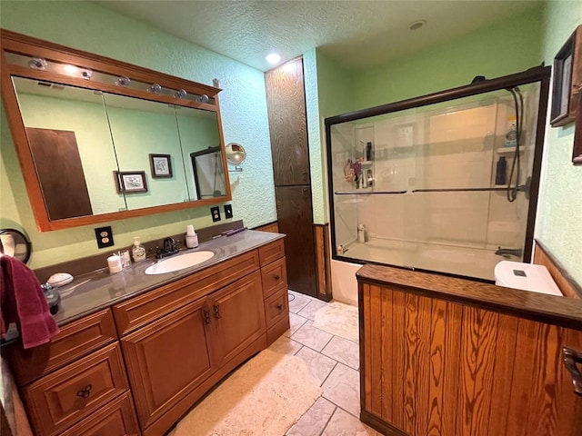 bathroom with a textured ceiling, vanity, and bath / shower combo with glass door